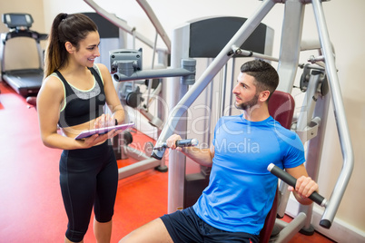 Trainer working with athlete at weights machine