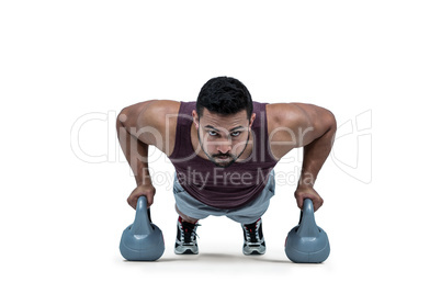 Muscular man doing push ups with kettlebells