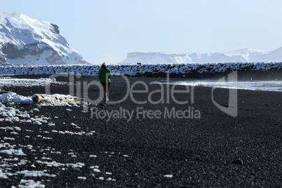 Woman walks along black sand beach in Vik, Iceland