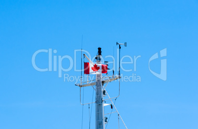 Top of metal ship mast with Canadian flag on blue sky