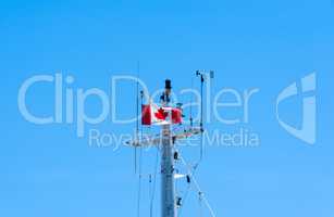 Top of metal ship mast with Canadian flag on blue sky