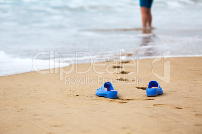 Beach Slippers and Blurred Silhouette of a Woman in Waves