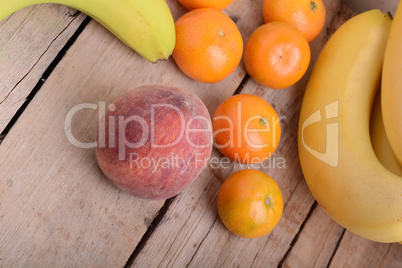 Bananas apple mandarin peach strawberry on wooden background as health food concept