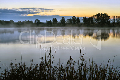 The morning landscape with sunrise over water in the fog