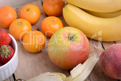 Bananas apple mandarin peach strawberry on wooden background as health food concept