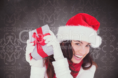 Composite image of happy brunette in santa hat holding gift