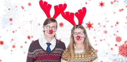 Composite image of portrait of smiling man and woman wearing red reindeer horn