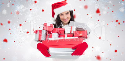 Composite image of smiling brunette in santa hat holding stack of presents