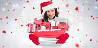 Composite image of smiling brunette in santa hat holding stack of presents