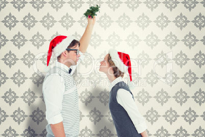 Composite image of geeky hipster kissing under mistletoe