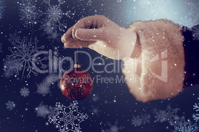 Composite image of santas hand is holding a christmas bulb