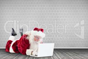 Composite image of santa lies in front of his laptop