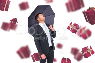 Composite image of businessman sheltering under black umbrella