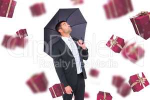 Composite image of businessman sheltering under black umbrella