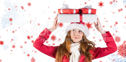 Composite image of festive redhead holding pile of gifts