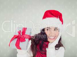 Composite image of surprised brunette in santa hat holding gift