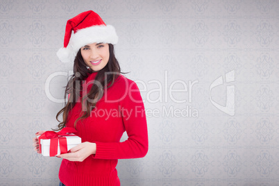 Composite image of smiling brunette in santa hat holding a gift