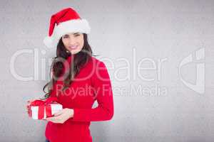 Composite image of smiling brunette in santa hat holding a gift