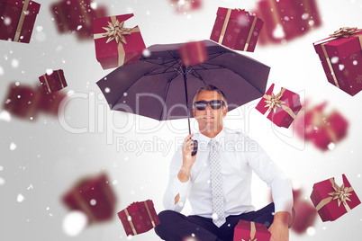 Composite image of businessman holding umbrella while sitting on