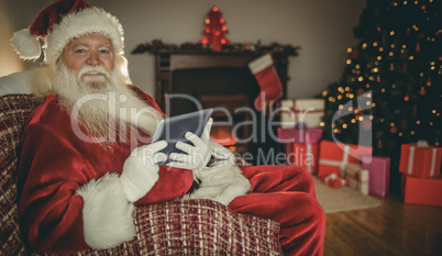 Cheerful santa using tablet on the couch