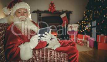 Cheerful santa using tablet on the couch