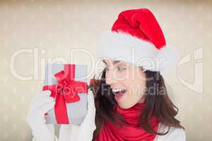 Composite image of astonished brunette in santa hat showing gift