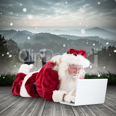 Composite image of santa lies in front of his laptop