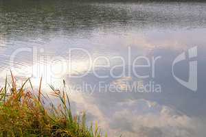 Autumn water background with reflection of clouds in water and g