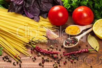 Raw pasta, vegetables, basil and spices on the wood table