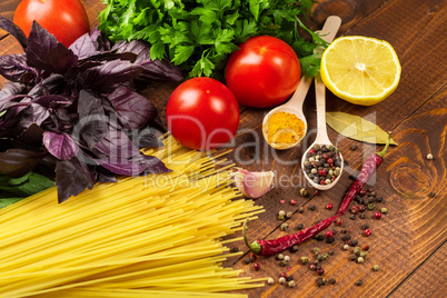 Raw pasta, vegetables, basil and spices on the wood table