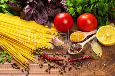 Raw pasta, vegetables, basil and spices on the wood table