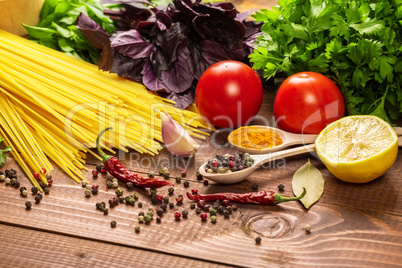 Raw pasta, vegetables, basil and spices on the wood table