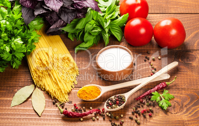 Raw pasta, vegetables, basil and spices on the wood table