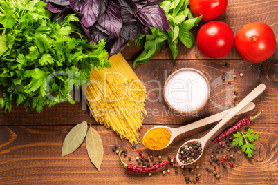 Raw pasta, vegetables, basil and spices on the wood table