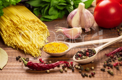 Raw pasta, vegetables, basil and spices on the wood table