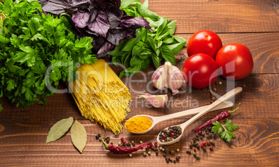 Raw pasta, vegetables, basil and spices on the wood table