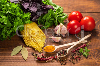 Raw pasta, vegetables, basil and spices on the wood table