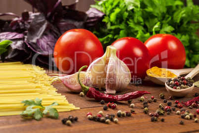 Raw pasta, vegetables, basil and spices on the wood table