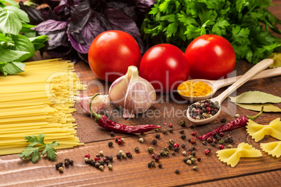 Raw pasta, vegetables, basil and spices on the wood table