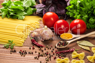 Raw pasta, vegetables, basil and spices on the wood table