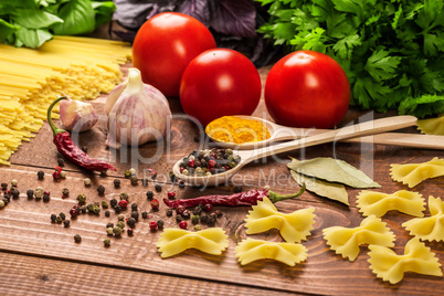 Raw pasta, vegetables, basil and spices on the wood table