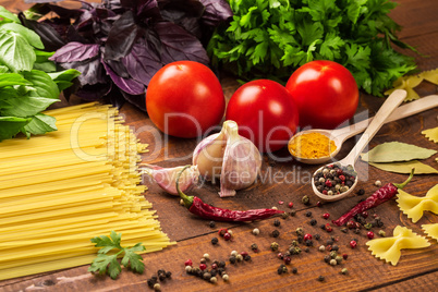 Raw pasta, vegetables, basil and spices on the wood table