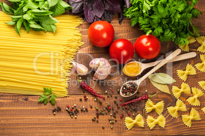 Raw pasta, vegetables, basil and spices on the wood table