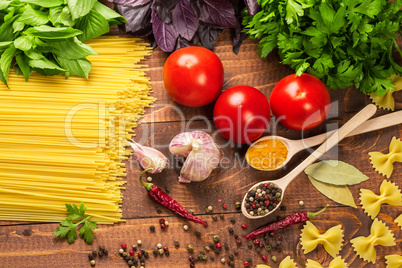 Raw pasta, vegetables, basil and spices on the wood table