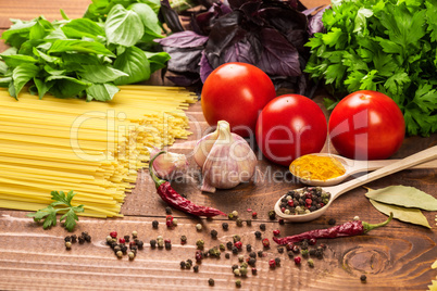 Raw pasta, vegetables, basil and spices on the wood table