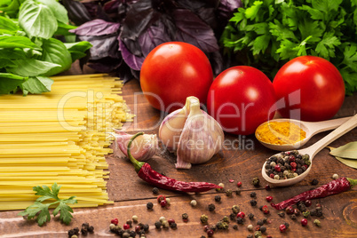 Raw pasta, vegetables, basil and spices on the wood table