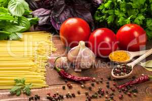 Raw pasta, vegetables, basil and spices on the wood table