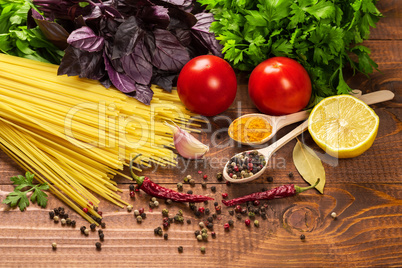 Raw pasta, vegetables, basil and spices on the wood table