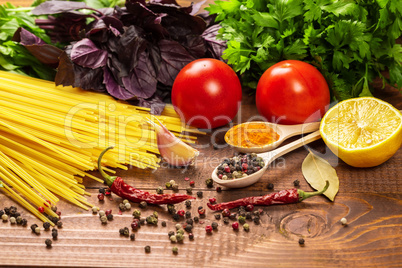 Raw pasta, vegetables, basil and spices on the wood table