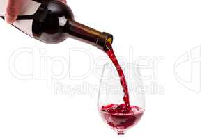 Red wine pouring from bottle into big glass on white background